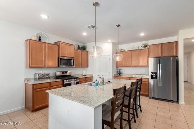 kitchen featuring a center island with sink, stainless steel appliances, hanging light fixtures, a kitchen bar, and sink