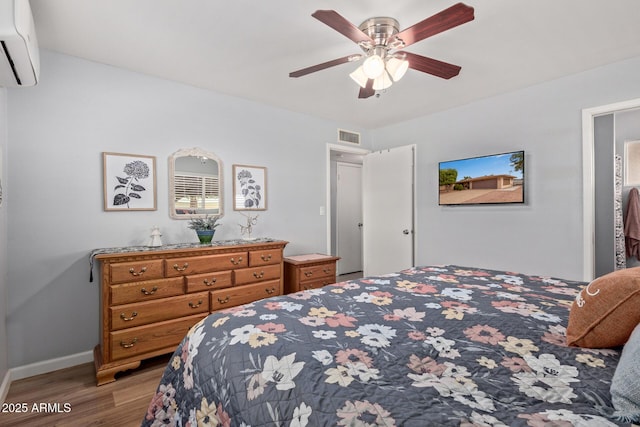 bedroom with visible vents, baseboards, wood finished floors, a wall mounted AC, and a ceiling fan