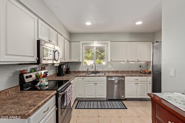 kitchen with a sink, dark countertops, white cabinetry, stainless steel appliances, and light tile patterned flooring