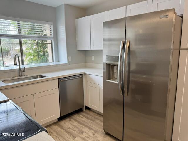 kitchen with white cabinetry, sink, stainless steel appliances, and light hardwood / wood-style floors