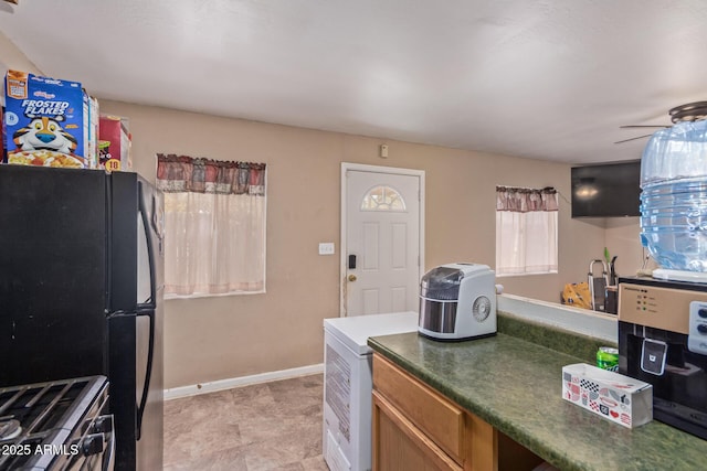 kitchen with freestanding refrigerator, dark countertops, stainless steel gas range oven, and baseboards