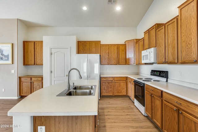 kitchen featuring sink, an island with sink, light hardwood / wood-style floors, and white appliances