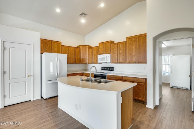 kitchen with white appliances, high vaulted ceiling, a center island with sink, sink, and light wood-type flooring