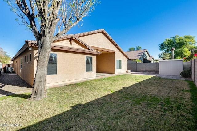 rear view of property featuring a lawn and a storage unit