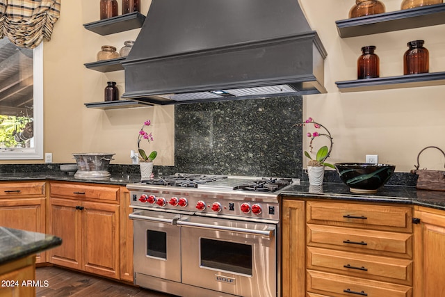 kitchen featuring range with two ovens, tasteful backsplash, dark stone countertops, custom exhaust hood, and dark hardwood / wood-style floors