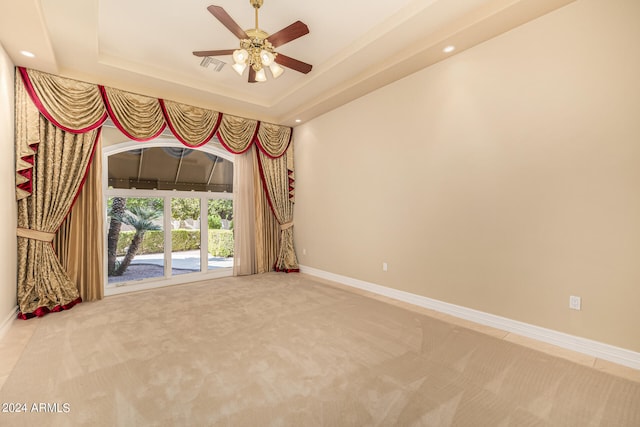 carpeted spare room featuring a tray ceiling and ceiling fan