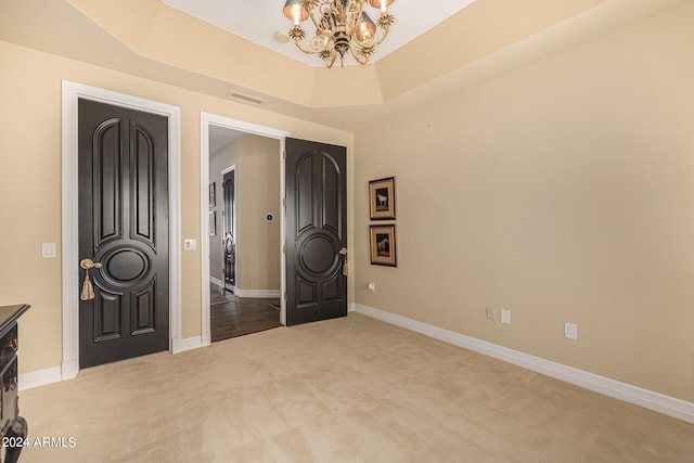 unfurnished bedroom featuring light colored carpet, an inviting chandelier, and a raised ceiling