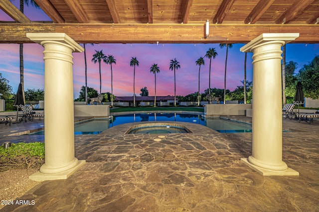 pool at dusk featuring an in ground hot tub and a patio area