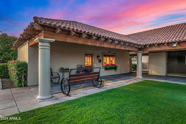 back house at dusk featuring a yard and a patio area