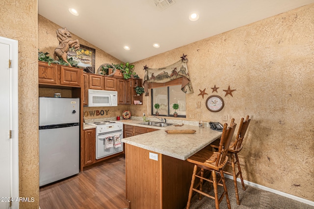 kitchen with white appliances, a breakfast bar, lofted ceiling, kitchen peninsula, and dark hardwood / wood-style floors