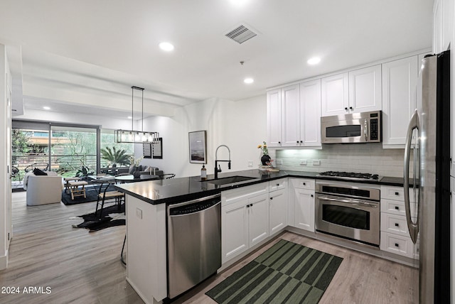 kitchen with light hardwood / wood-style floors, stainless steel appliances, kitchen peninsula, white cabinetry, and sink