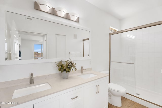 bathroom with toilet, a stall shower, wood finished floors, and double vanity
