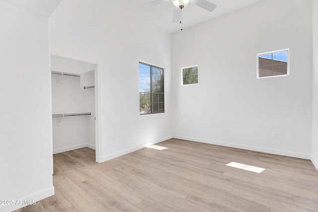 unfurnished bedroom featuring light wood-style floors, baseboards, a spacious closet, and a ceiling fan