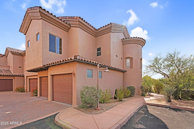 view of side of property with an attached garage, a tiled roof, stucco siding, and decorative driveway