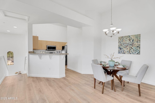 dining area featuring a towering ceiling, light wood finished floors, baseboards, and a chandelier