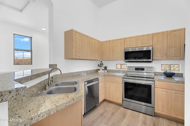 kitchen featuring stainless steel appliances, light brown cabinets, a sink, light wood finished floors, and light countertops