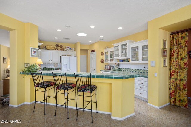 19714 N Concord Dr, Surprise, AZ 85374 - kitchen featuring white fridge with ice dispenser, tile countertops, a peninsula, a breakfast bar area, and white cabinets