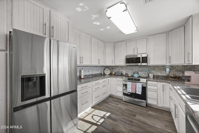 kitchen featuring dark hardwood / wood-style floors, decorative backsplash, dark stone countertops, white cabinetry, and stainless steel appliances