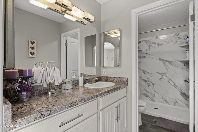 bathroom with vanity, toilet, a tile shower, and wood-type flooring