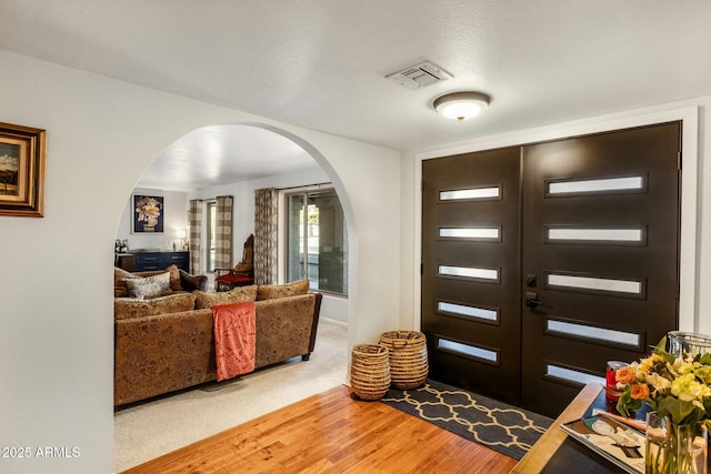 foyer featuring arched walkways, visible vents, and wood finished floors