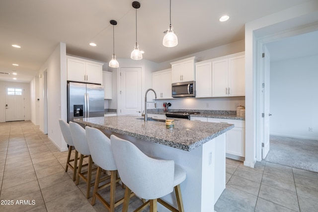 kitchen with light tile patterned flooring, stainless steel appliances, a breakfast bar, a sink, and an island with sink