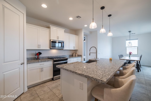 kitchen with range with electric cooktop, visible vents, an island with sink, stainless steel microwave, and a sink