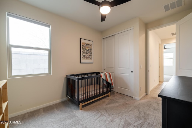 carpeted bedroom featuring ceiling fan, visible vents, baseboards, a closet, and a crib