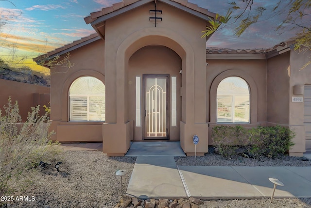 exterior entry at dusk featuring a tiled roof and stucco siding