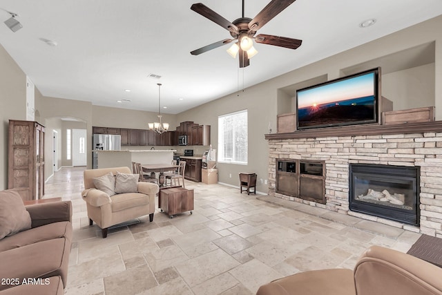 living room featuring arched walkways, a stone fireplace, ceiling fan with notable chandelier, visible vents, and baseboards