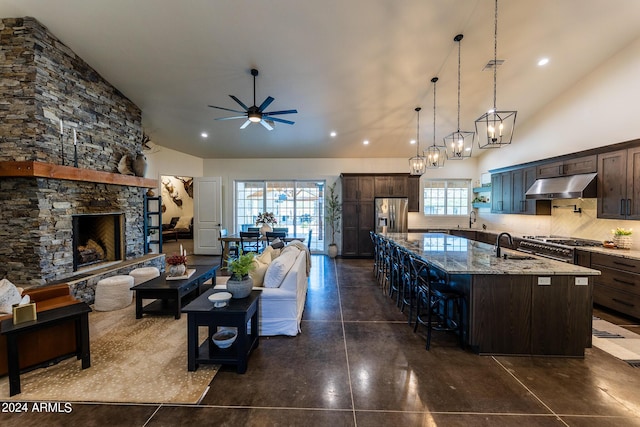 kitchen with stainless steel refrigerator with ice dispenser, a spacious island, dark brown cabinetry, light stone counters, and decorative backsplash