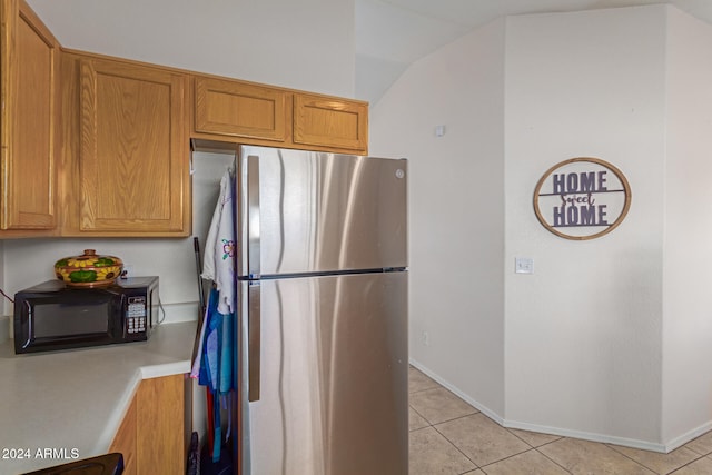 kitchen with vaulted ceiling, stainless steel refrigerator, and light tile patterned flooring