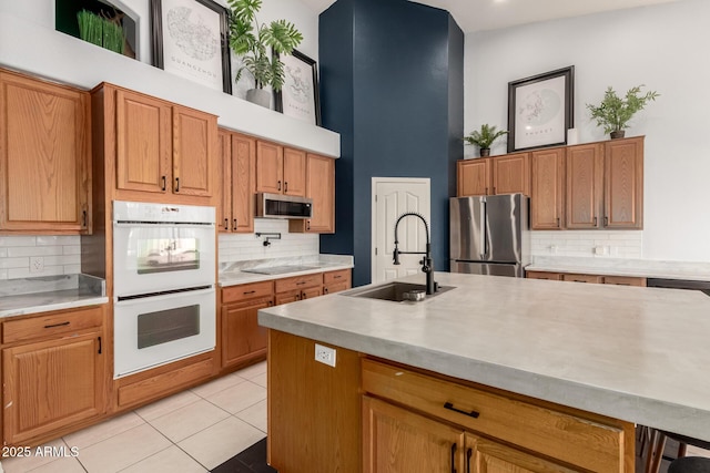 kitchen featuring a sink, appliances with stainless steel finishes, a high ceiling, decorative backsplash, and light countertops