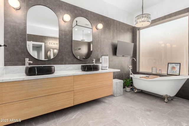 bathroom featuring tile walls, double vanity, marble finish floors, and a soaking tub