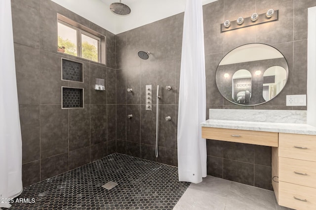 bathroom featuring tile patterned flooring, a tile shower, vanity, and tile walls