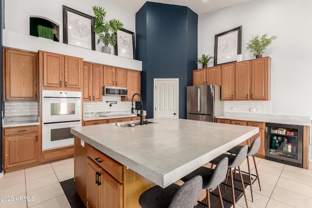 kitchen featuring beverage cooler, stainless steel appliances, a sink, a high ceiling, and light tile patterned floors