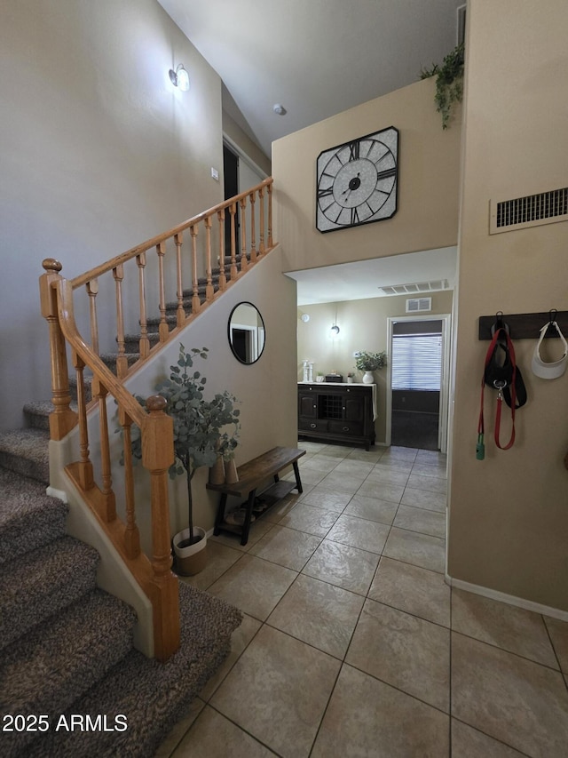 staircase featuring tile patterned floors, a towering ceiling, visible vents, and baseboards