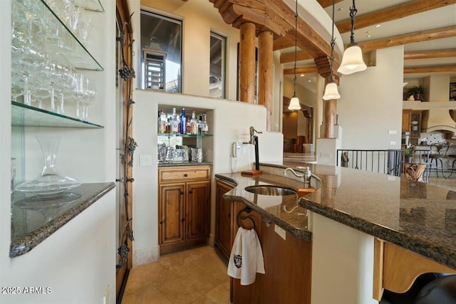 kitchen with pendant lighting, brown cabinetry, a sink, dark stone counters, and beamed ceiling