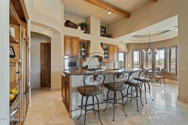 kitchen with arched walkways, appliances with stainless steel finishes, brown cabinets, custom exhaust hood, and a notable chandelier