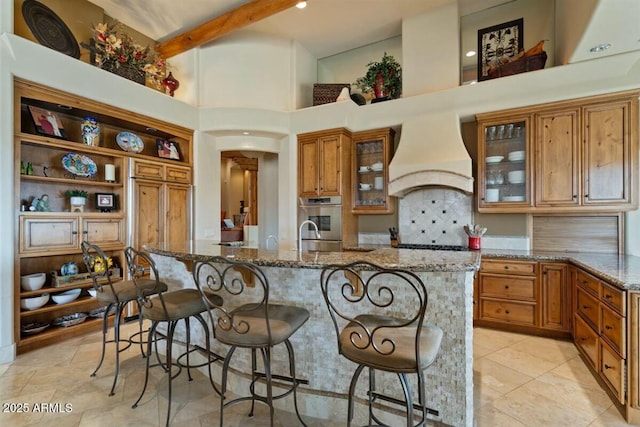 kitchen with a kitchen breakfast bar, stone counters, custom exhaust hood, and brown cabinets