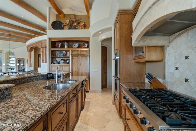 kitchen featuring arched walkways, brown cabinetry, range hood, stainless steel gas cooktop, and a sink