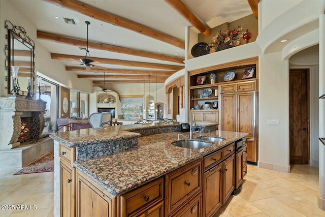 kitchen featuring arched walkways, a premium fireplace, brown cabinetry, stone countertops, and a sink