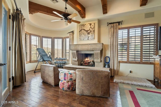 living room featuring a warm lit fireplace, visible vents, dark wood finished floors, a ceiling fan, and beam ceiling