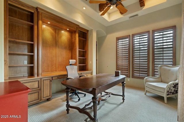 home office featuring ceiling fan, built in shelves, light colored carpet, visible vents, and a raised ceiling