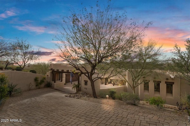 back of house at dusk with a fenced front yard and decorative driveway