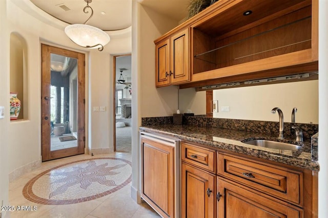 kitchen featuring open shelves, visible vents, brown cabinetry, a sink, and dark stone counters