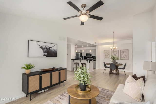 living room with a chandelier, light wood finished floors, vaulted ceiling, a ceiling fan, and baseboards