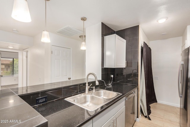 kitchen with a sink, stainless steel appliances, white cabinetry, pendant lighting, and decorative backsplash