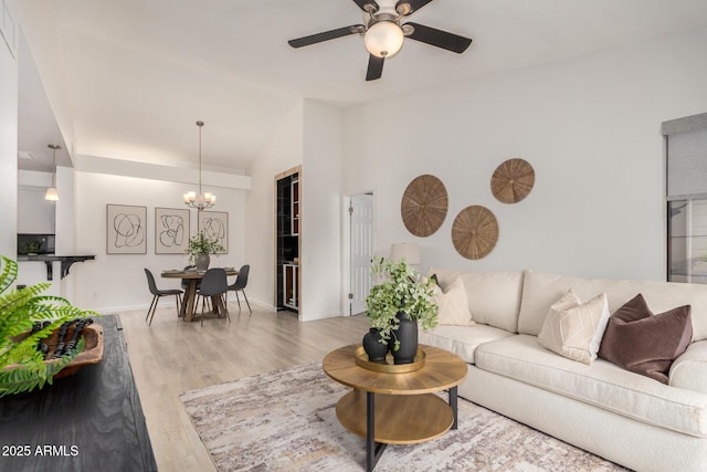 living room featuring a chandelier, a ceiling fan, wood finished floors, baseboards, and high vaulted ceiling