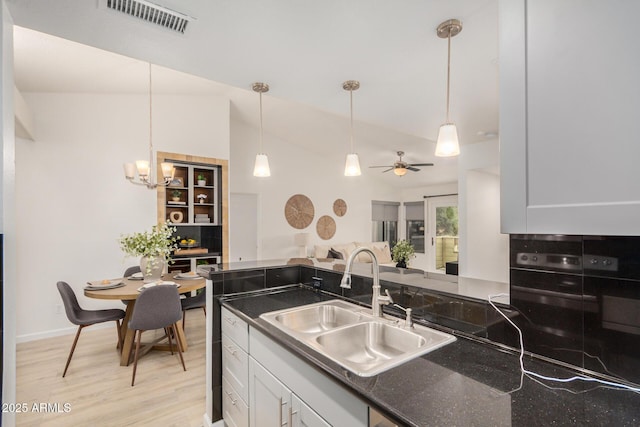 kitchen with a sink, light wood-type flooring, white cabinetry, decorative light fixtures, and a peninsula