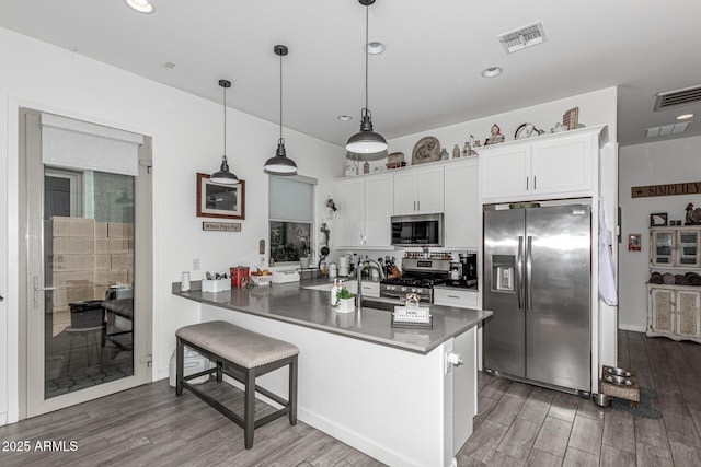 kitchen featuring a breakfast bar, white cabinetry, appliances with stainless steel finishes, kitchen peninsula, and pendant lighting